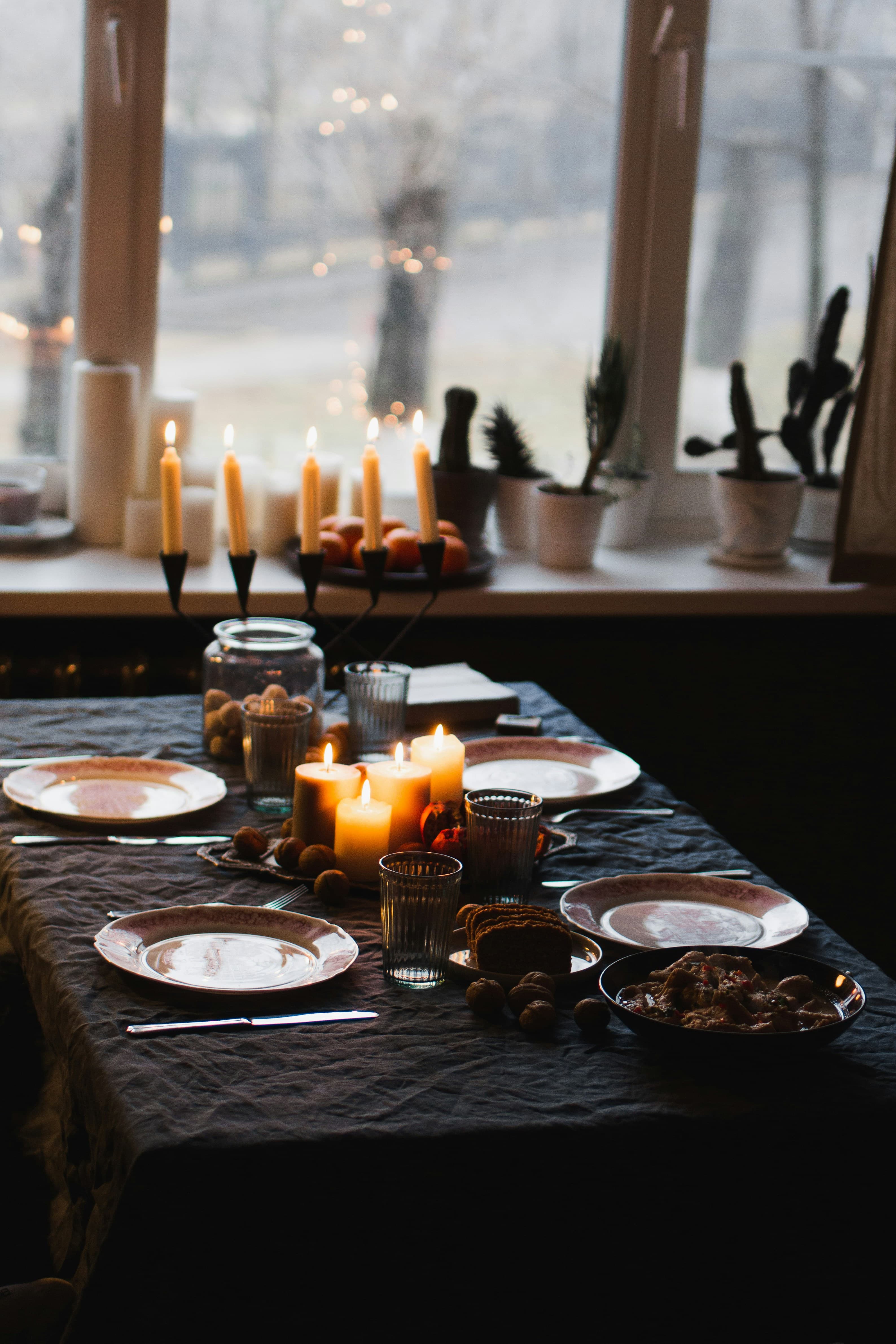 A long table set by the window, candles burning, evening light outside